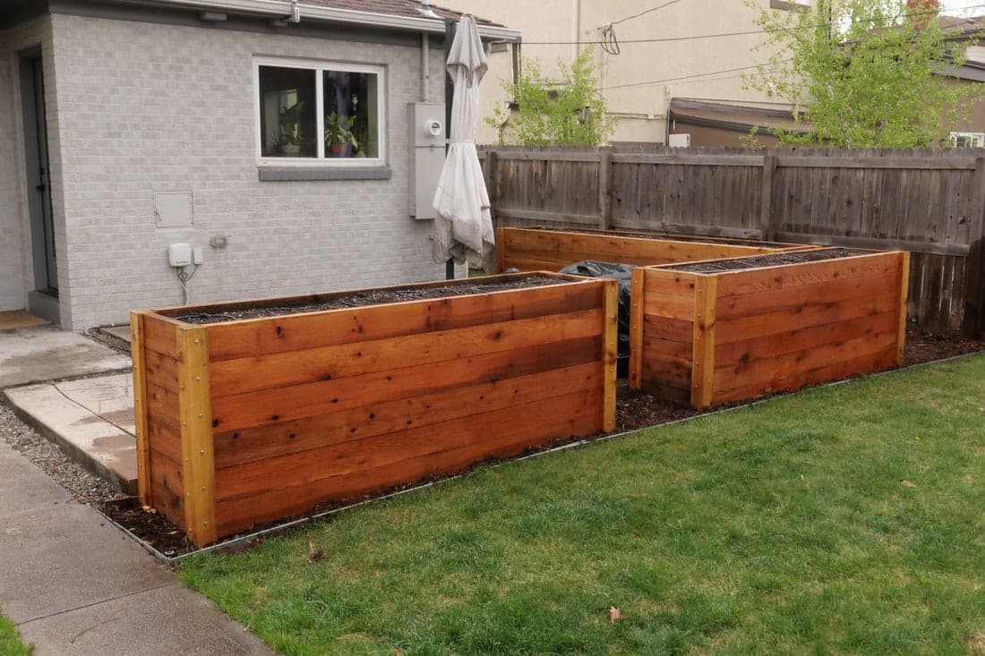 Tall cedar raised beds lined up along a brick garage wall beside a lawn
