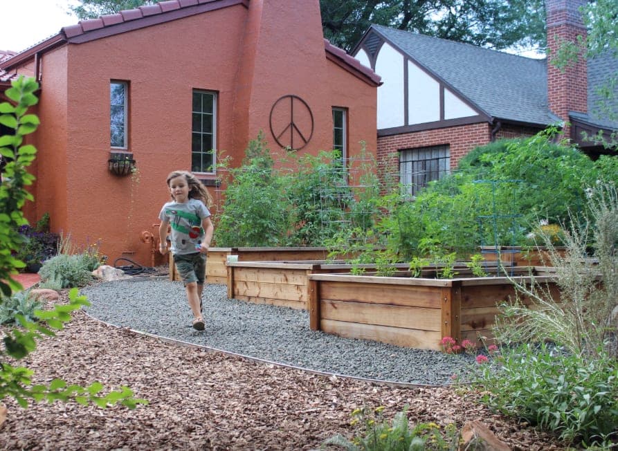 Child running along a gravel path past cedar raised beds in a front yard